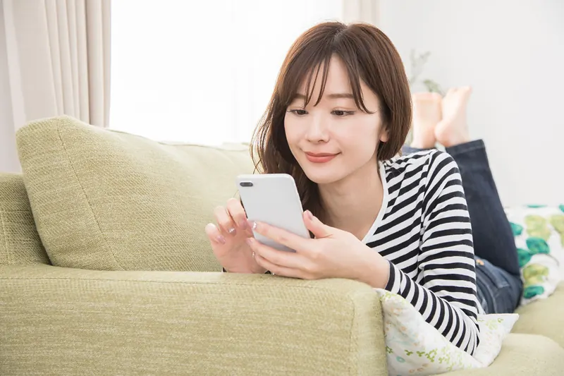 自宅のソファでスマートフォンから賃貸物件を探す女性